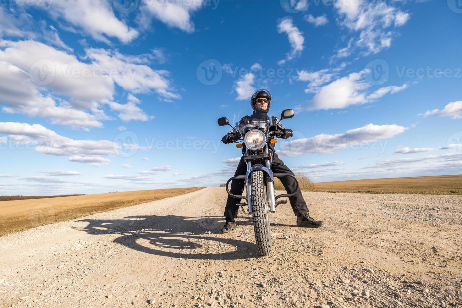 man i en svart enhetlig på cykel mot de bakgrund av panorama av fält och blå himmel. motorcykel resa begrepp foto