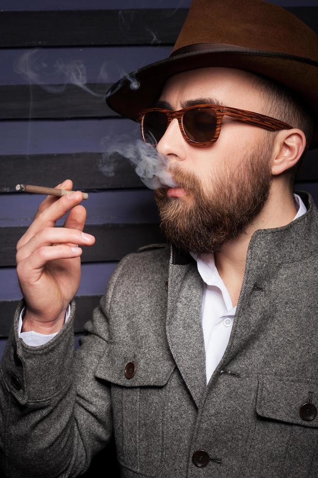 Häftigt stilig rökning. sida se av stilig ung man i solglasögon rökning en cigarett foto