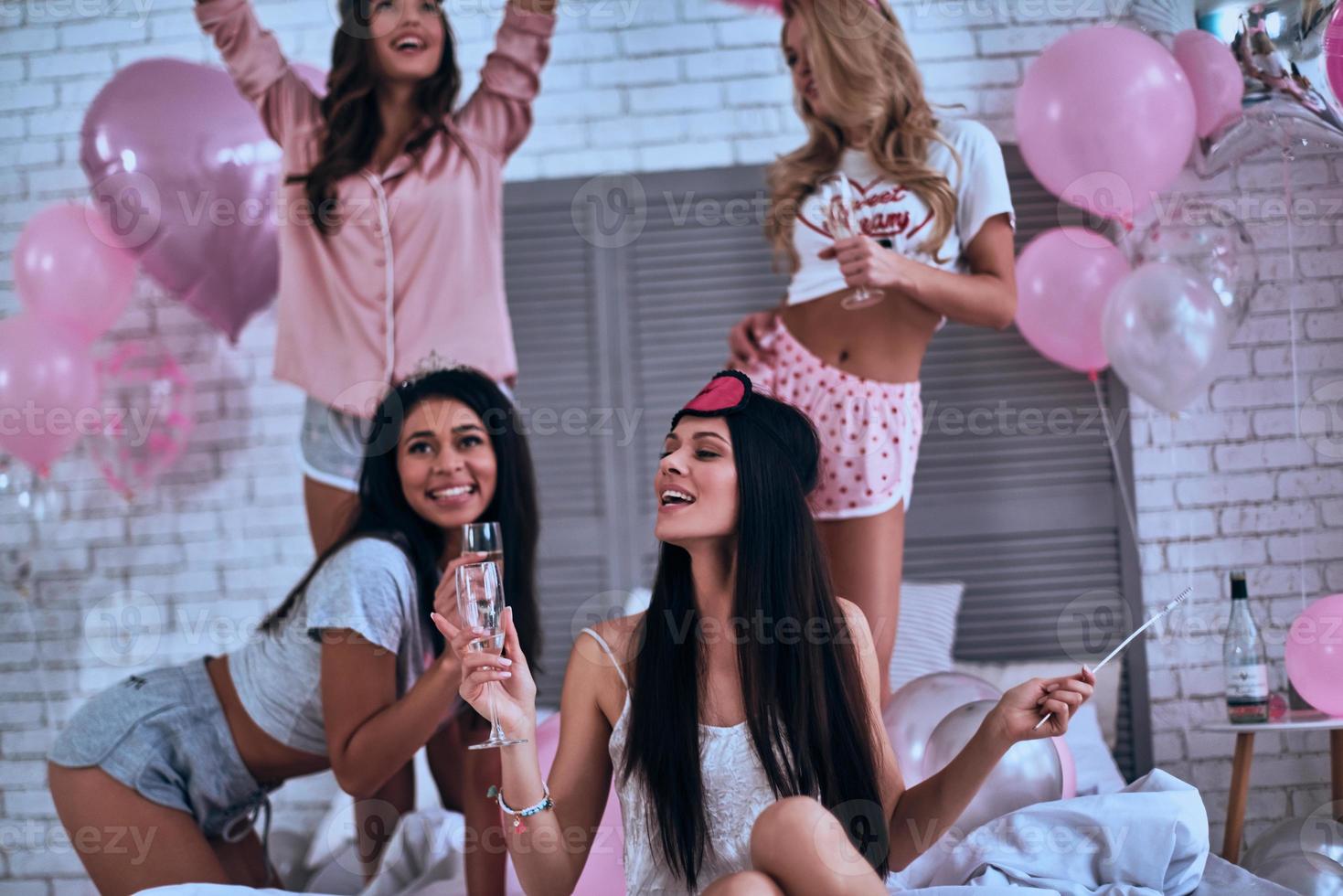lämna Allt de oro Bakom. fyra attraktiv ung leende kvinnor i pyjamas dricka champagne medan har en slummer fest foto