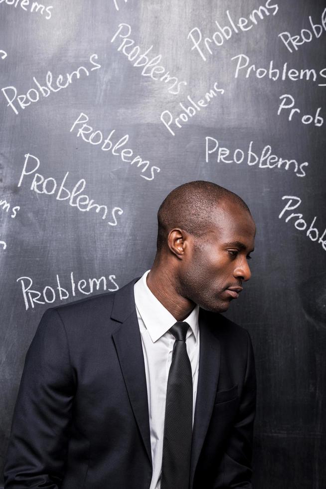 problem Allt runt om mig. deprimerad afrikansk man i formell klädsel stående mot svarta tavlan med inskrift problem foto