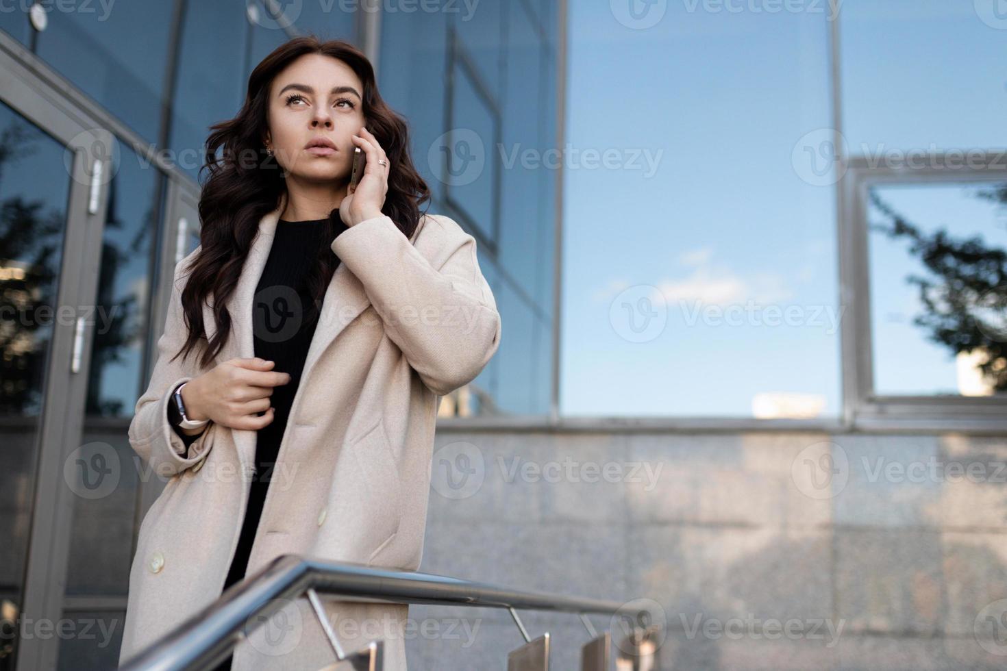 ung affärskvinna talande på en mobil telefon mot de bakgrund av ett kontor byggnad, karriär tillväxt begrepp foto