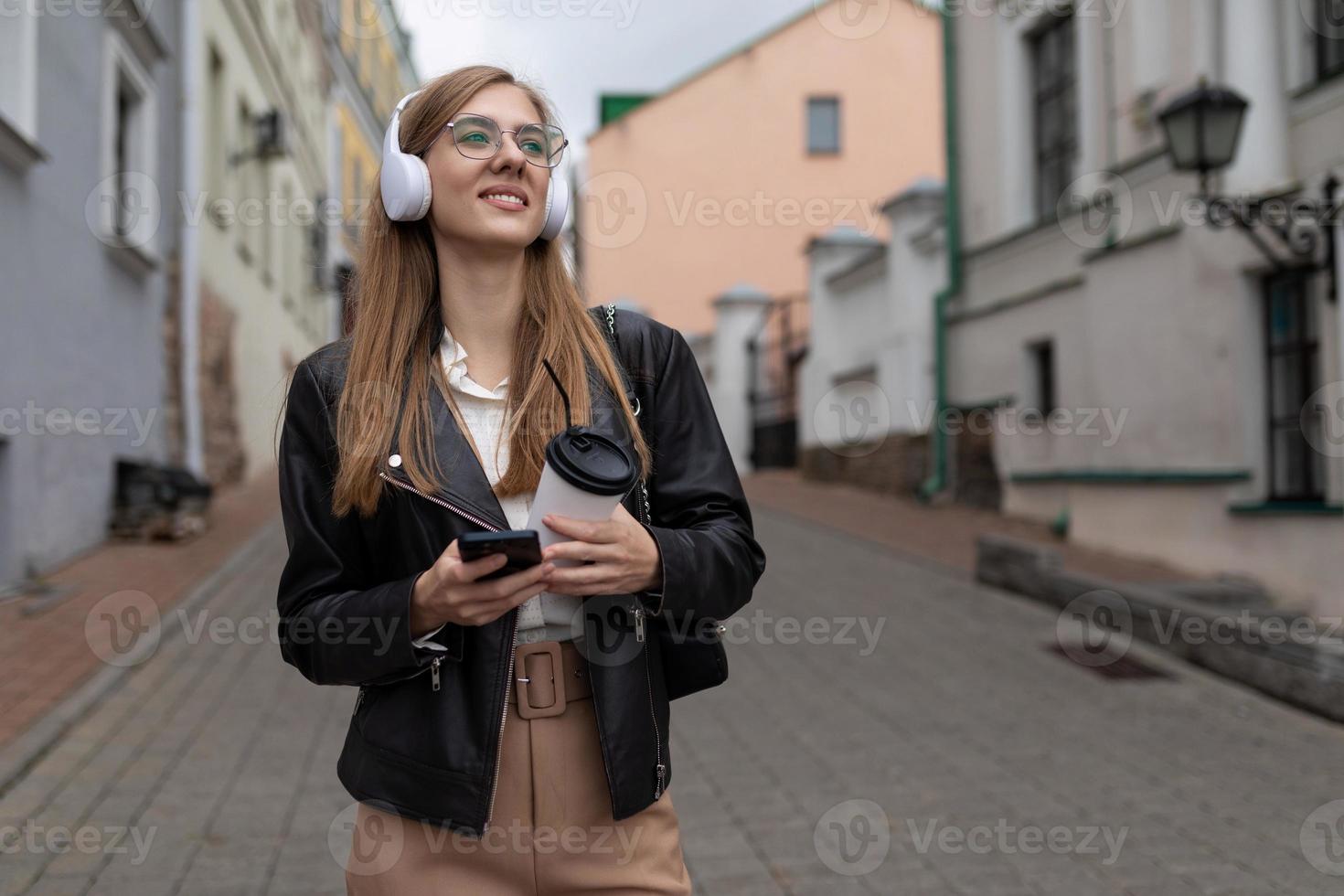 ung kvinna turist i hörlurar med en mobil telefon promenader genom de gammal stad foto