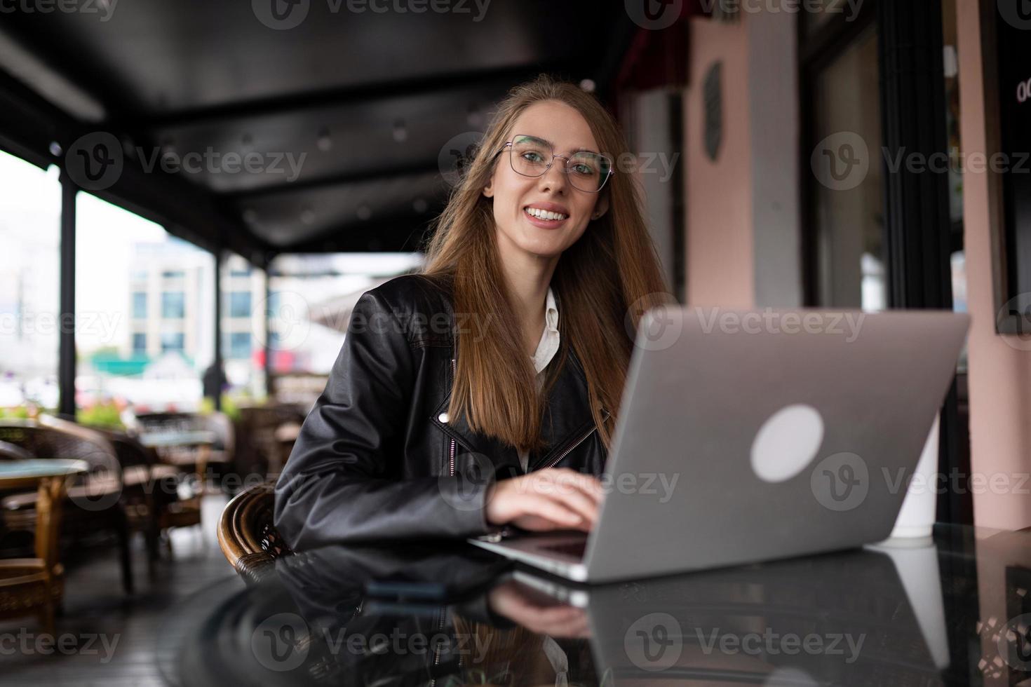 ung eleganta kvinna sitter på de trappa Nästa till en populär Kafé med en kopp av kaffe och klockor en mobil telefon foto