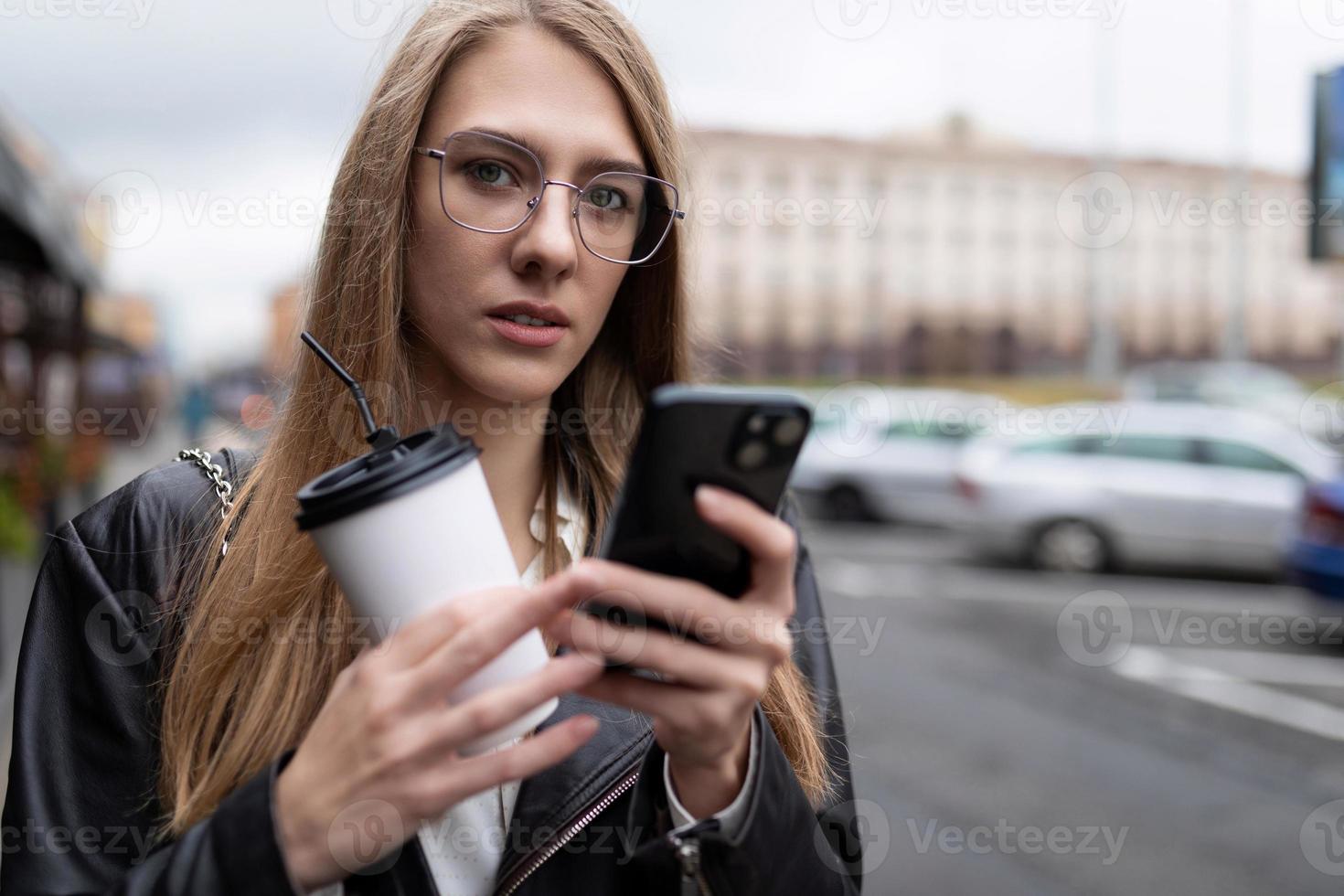 porträtt av en allvarlig ung kvinna med en kopp av kaffe ser på en mobil telefon foto