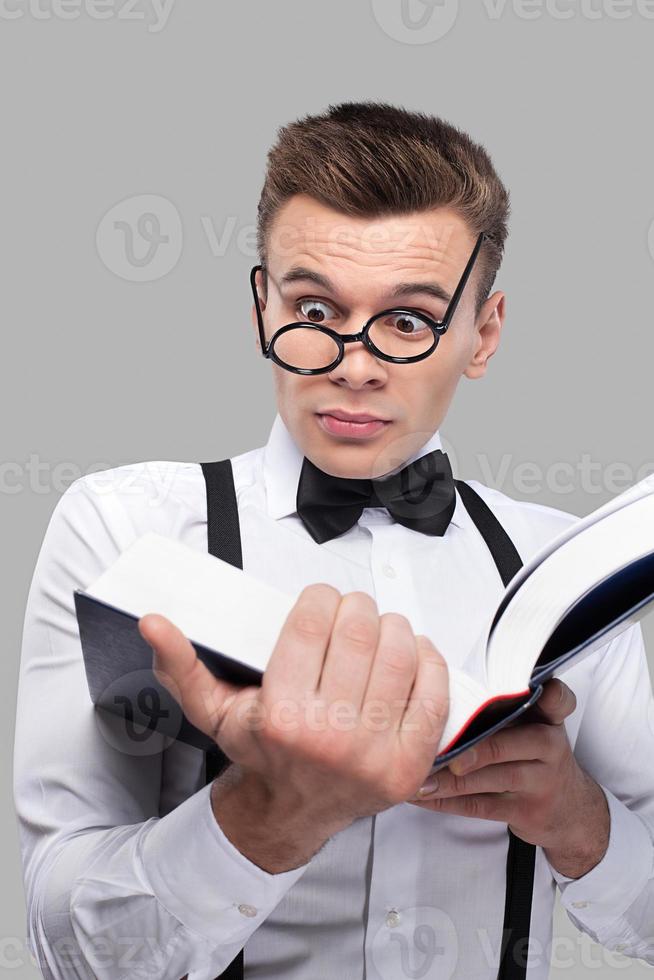 upprörande bok. chockade ung man i rosett slips och hängslen innehav läsning en bok medan stående mot grå bakgrund foto