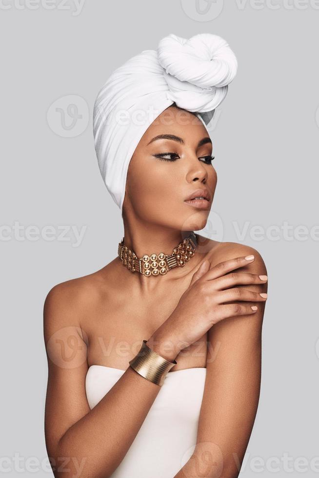 afrikansk skönhet. attraktiv ung afrikansk kvinna i turban ser bort medan stående mot grå bakgrund foto