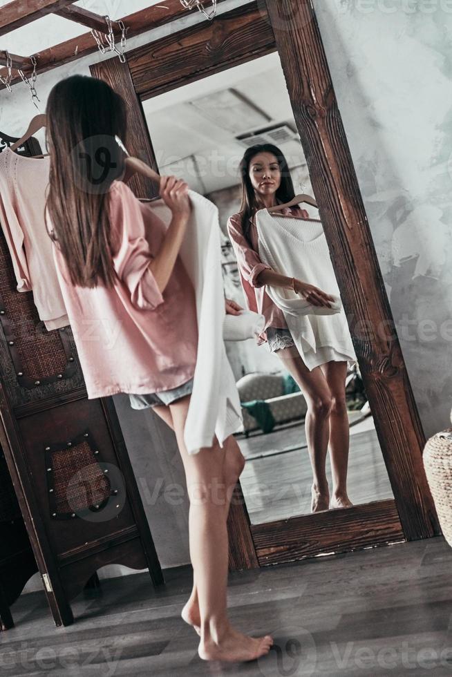 full längd av attraktiv ung kvinna påfrestande på de blus medan stående i främre av de spegel på Hem foto