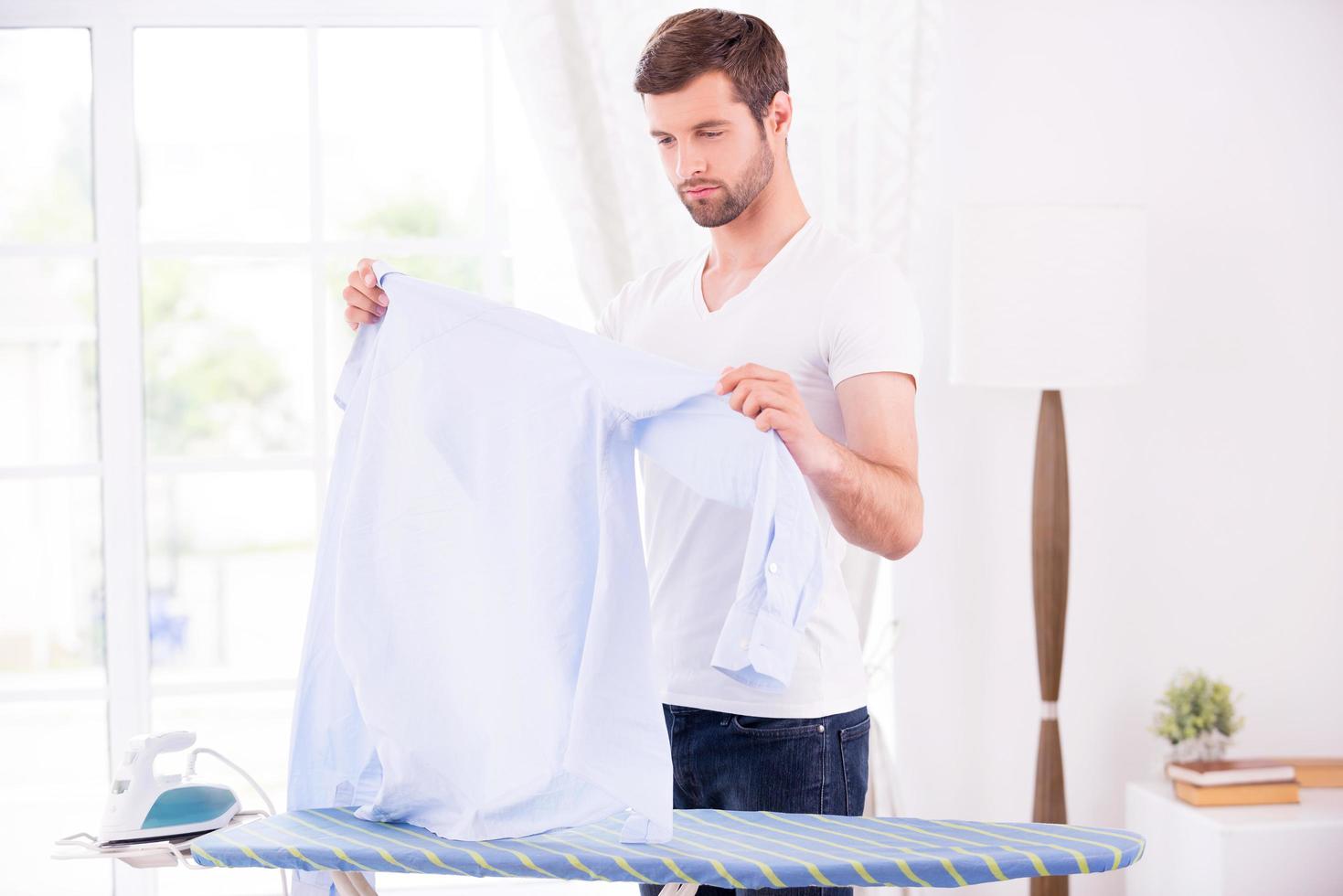 framställning till strykning. självsäker ung man granskning hans skjorta innan strykning foto