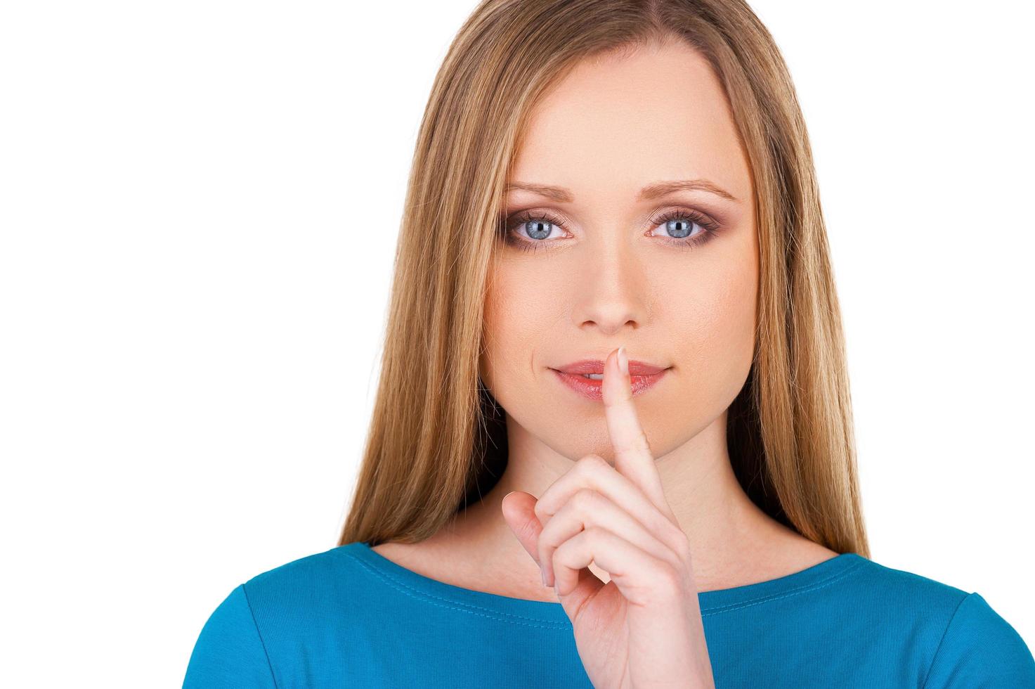 förvaring tystnad. attraktiv ung kvinna ser på kamera och innehav finger på mun medan stående isolerat på vit foto