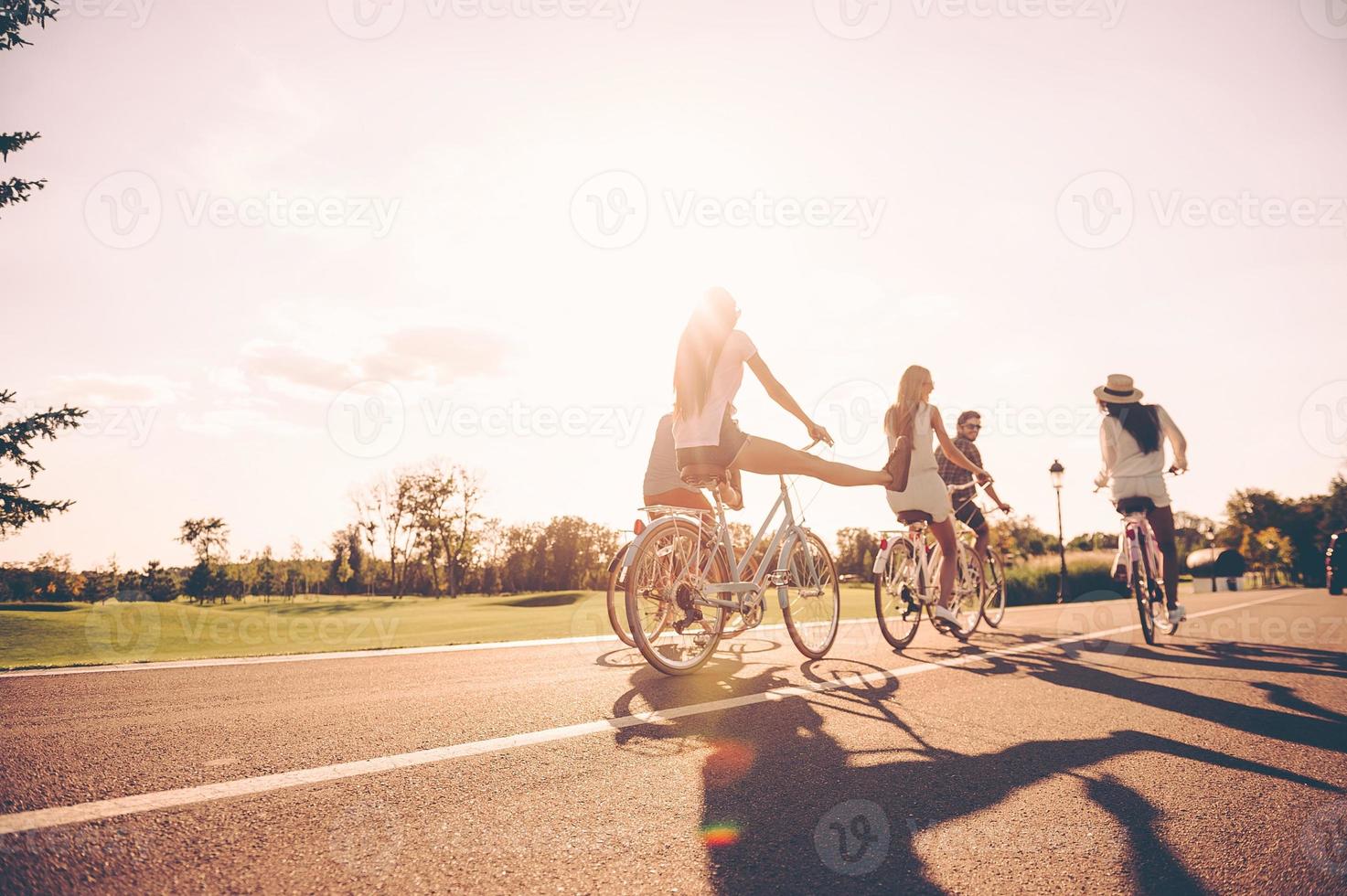 njuter trevlig sommar dag tillsammans. låg vinkel se av ung människor ridning cyklar längs en väg och ser Lycklig foto