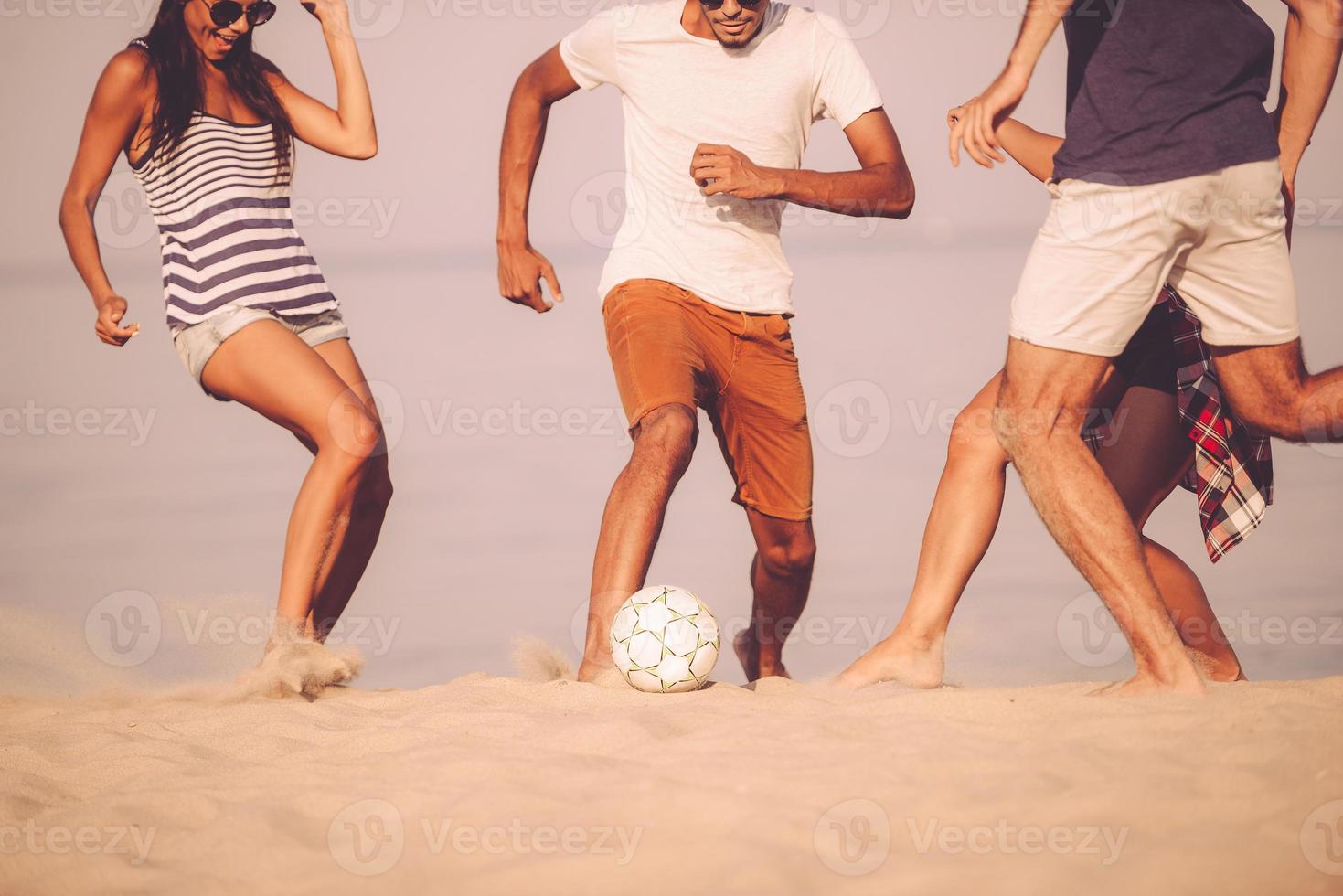 strand boll med vänner. beskurna bild av ung människor spelar med fotboll boll på de strand foto