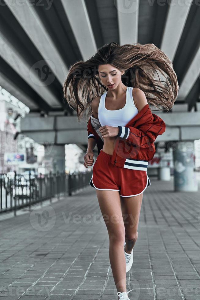utmanande själv. full längd av attraktiv ung kvinna i sport Kläder förvaring ögon stängd medan löpning under de bro utomhus foto