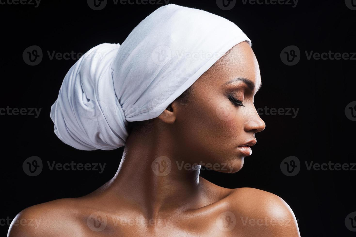 kombinerande skönhet och tradition. skön afrikansk kvinna bär en slöja och förvaring ögon stängd medan stående mot svart bakgrund foto