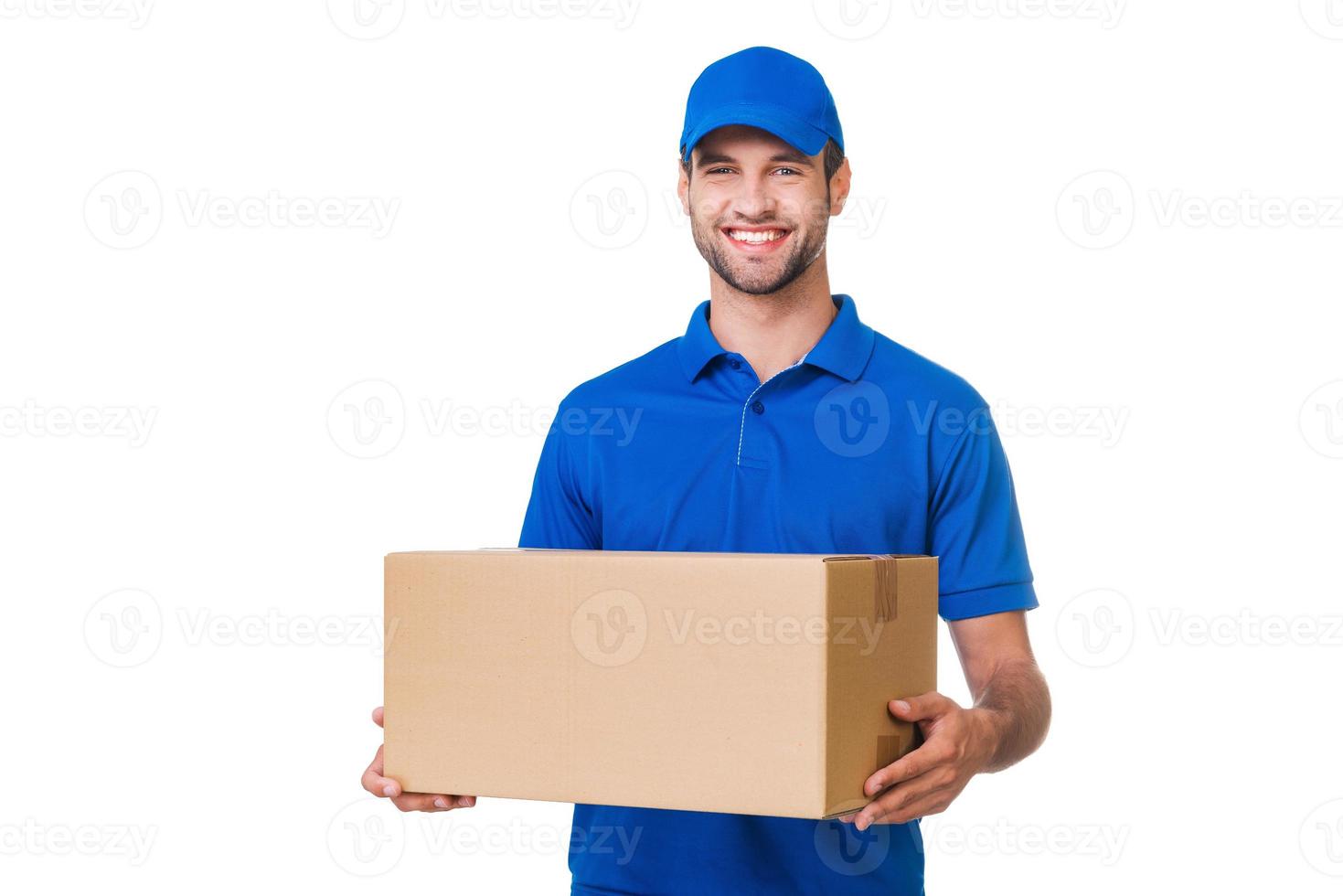 glad leverans man. Lycklig ung kurir innehav en kartong låda och leende medan stående mot vit bakgrund foto