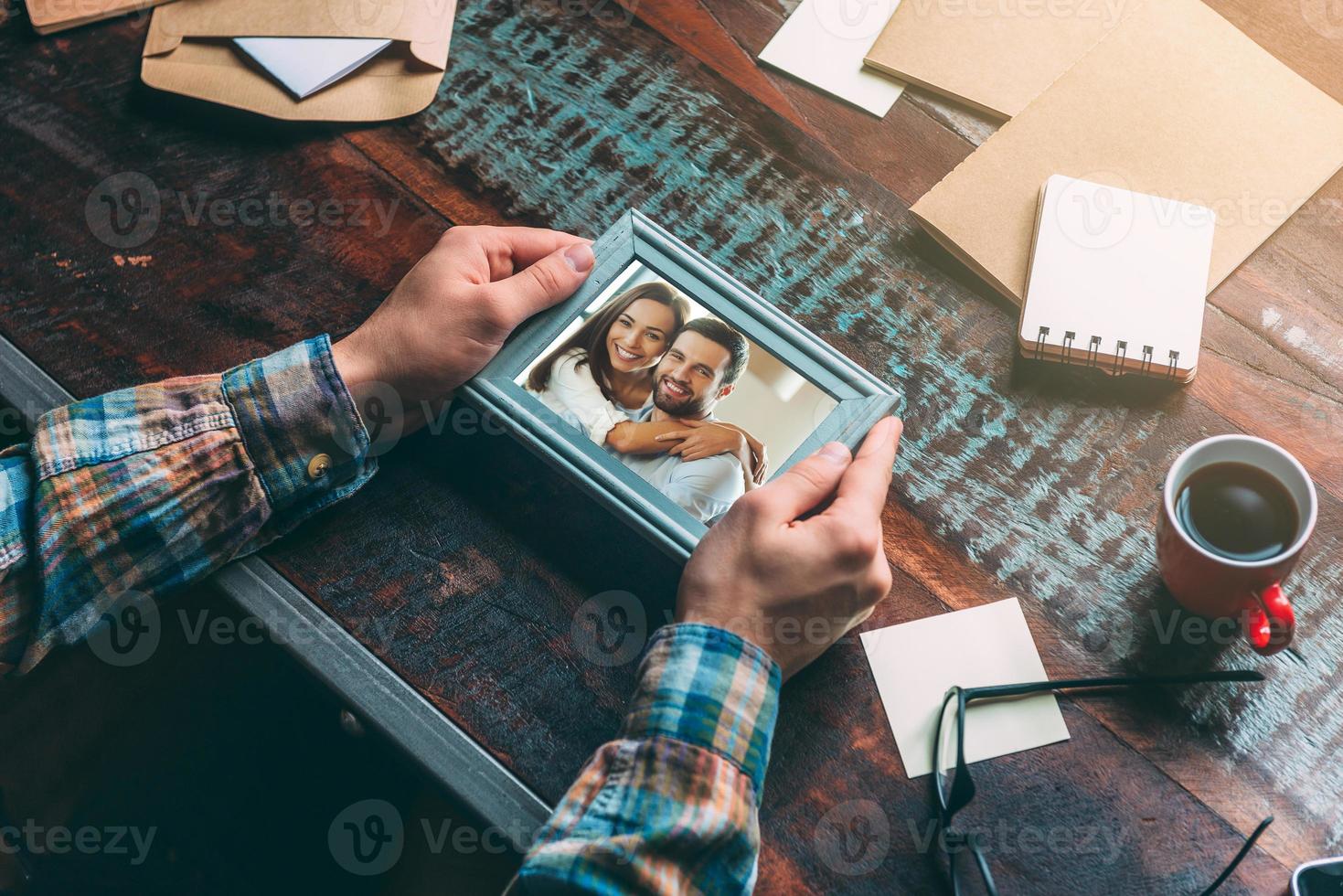 Bra minnen. närbild topp se bild av man innehav bild ram medan Sammanträde på de rustik trä- tabell foto