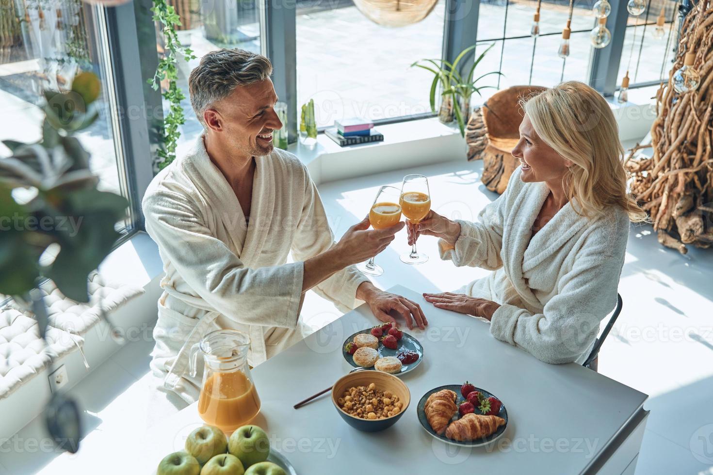 topp se av skön mogna par i morgonrockar njuter frukost tillsammans medan utgifterna tid i de inhemsk kök foto