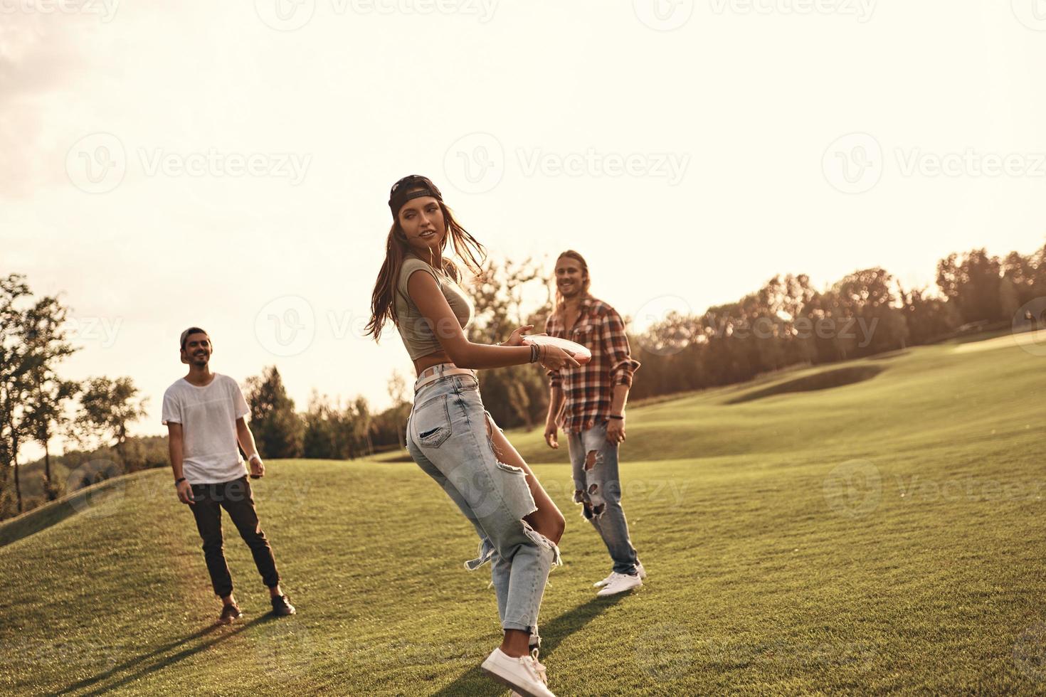 få redo till kasta. full längd av ung leende människor i tillfällig ha på sig spelar frisbee utomhus foto