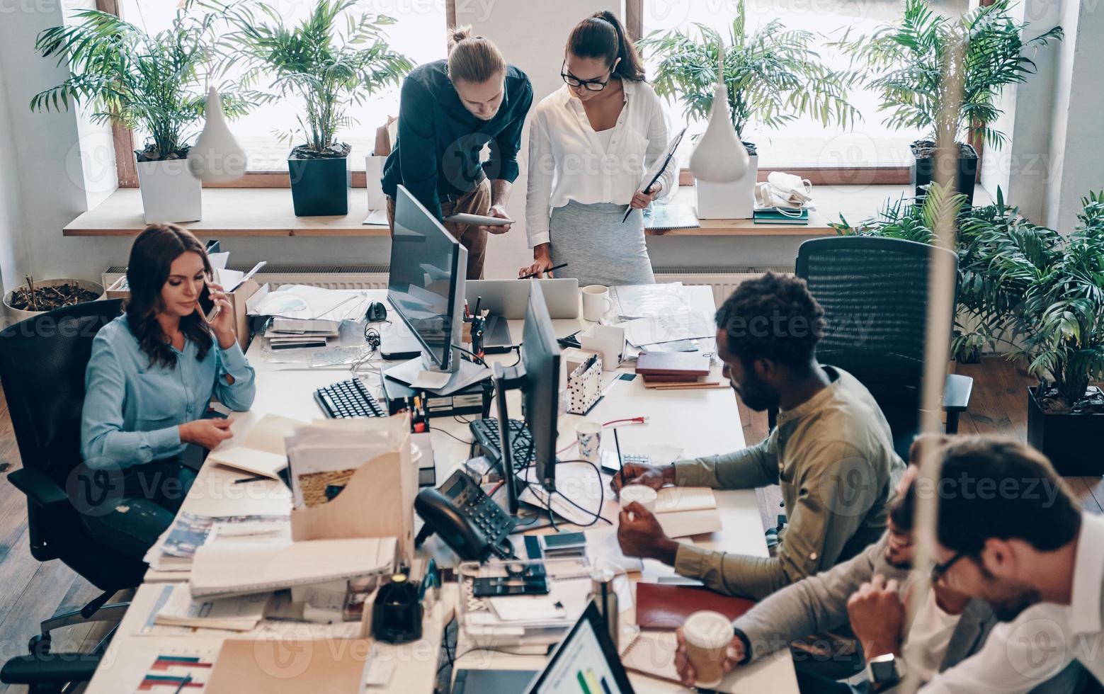 grupp av ung modern människor i smart tillfällig ha på sig kommunicerar och använder sig av modern teknik medan arbetssätt i de kontor foto