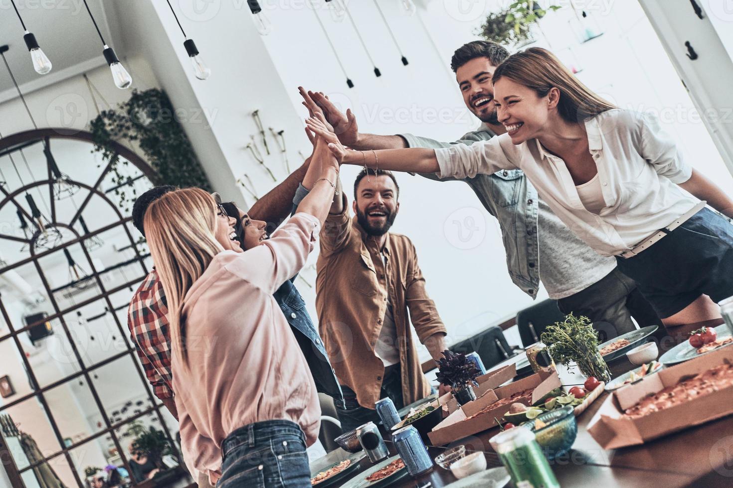 Lycklig vänner. grupp av ung människor ger varje Övrig hög femma i en symbol av enhet och leende medan har en middag fest foto