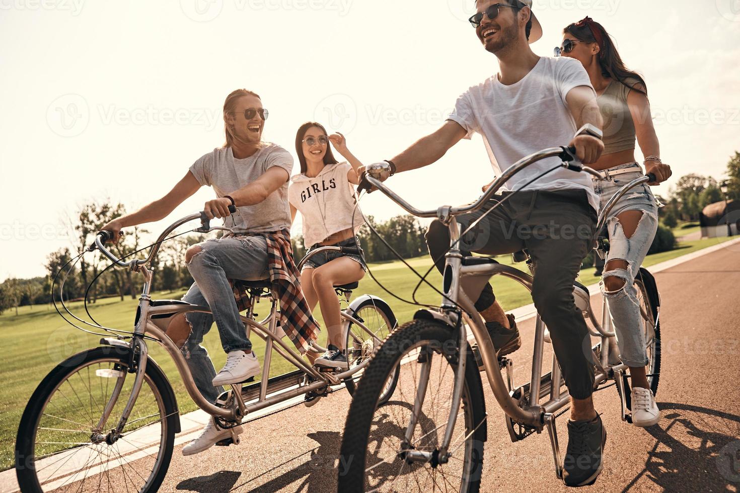 sorglös sommar dag. grupp av Lycklig ung människor i tillfällig ha på sig leende medan cykling tillsammans utomhus foto