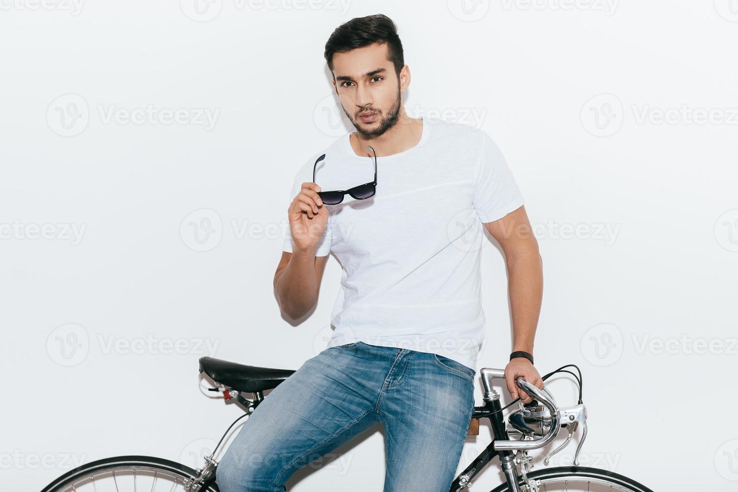 eleganta stilig. stilig ung indisk man lutande på hans retro styled cykel och ser på kamera medan stående mot vit bakgrund foto