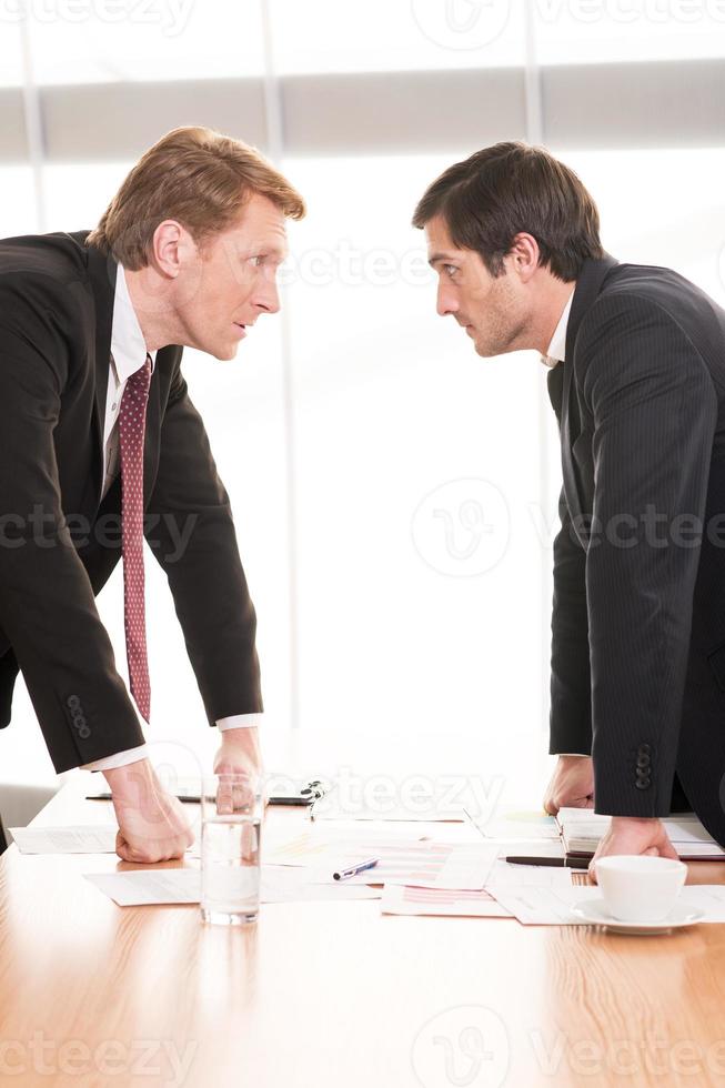 företag människor motstridig. två ung män i formell klädsel motstridig medan stående ansikte till ansikte foto