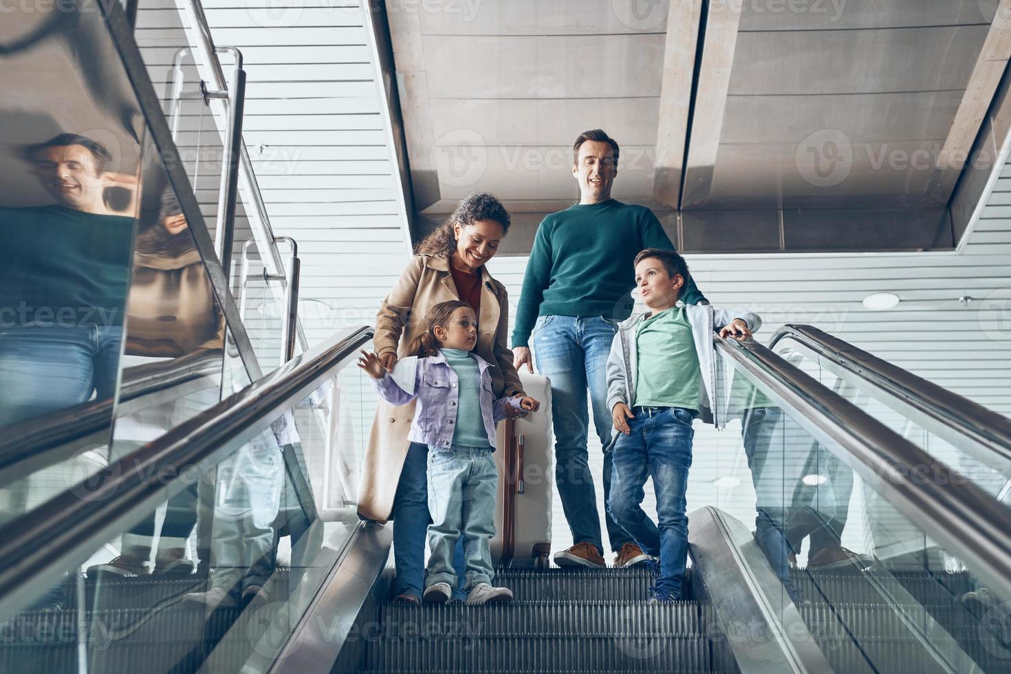 Lycklig familj med två liten barn rör på sig förbi rulltrappa i flygplats terminal foto