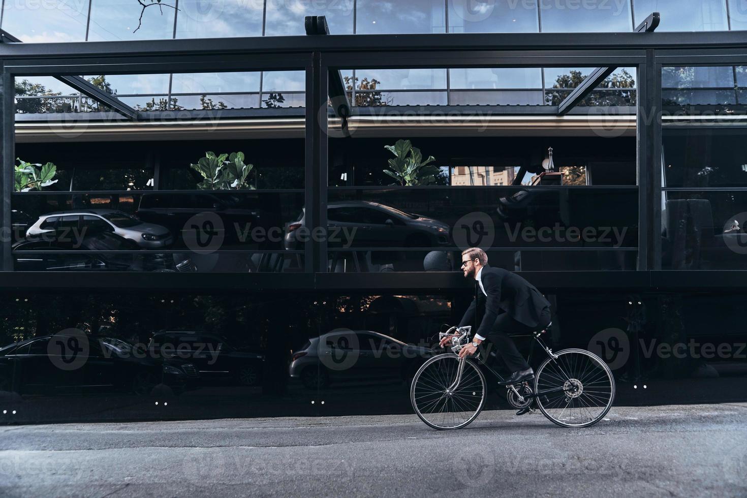 bekväm sätt till resa. stilig ung man i full kostym skyndar till arbete medan cykling utomhus foto