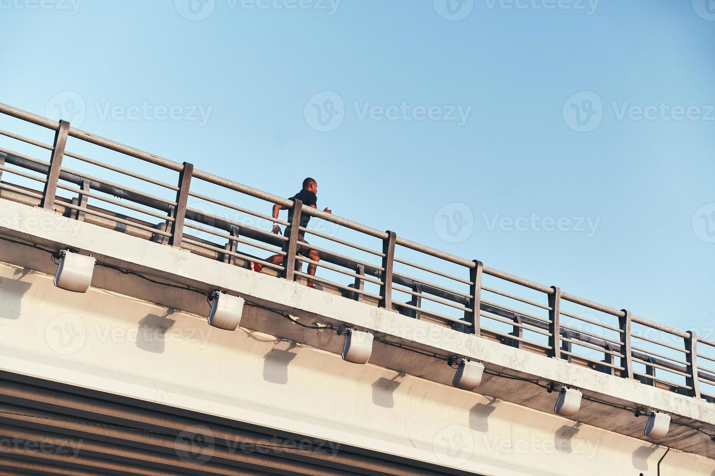 tryckande hård till vara de bäst. ung afrikansk man i sporter Kläder utövar medan löpning på de bro utomhus foto