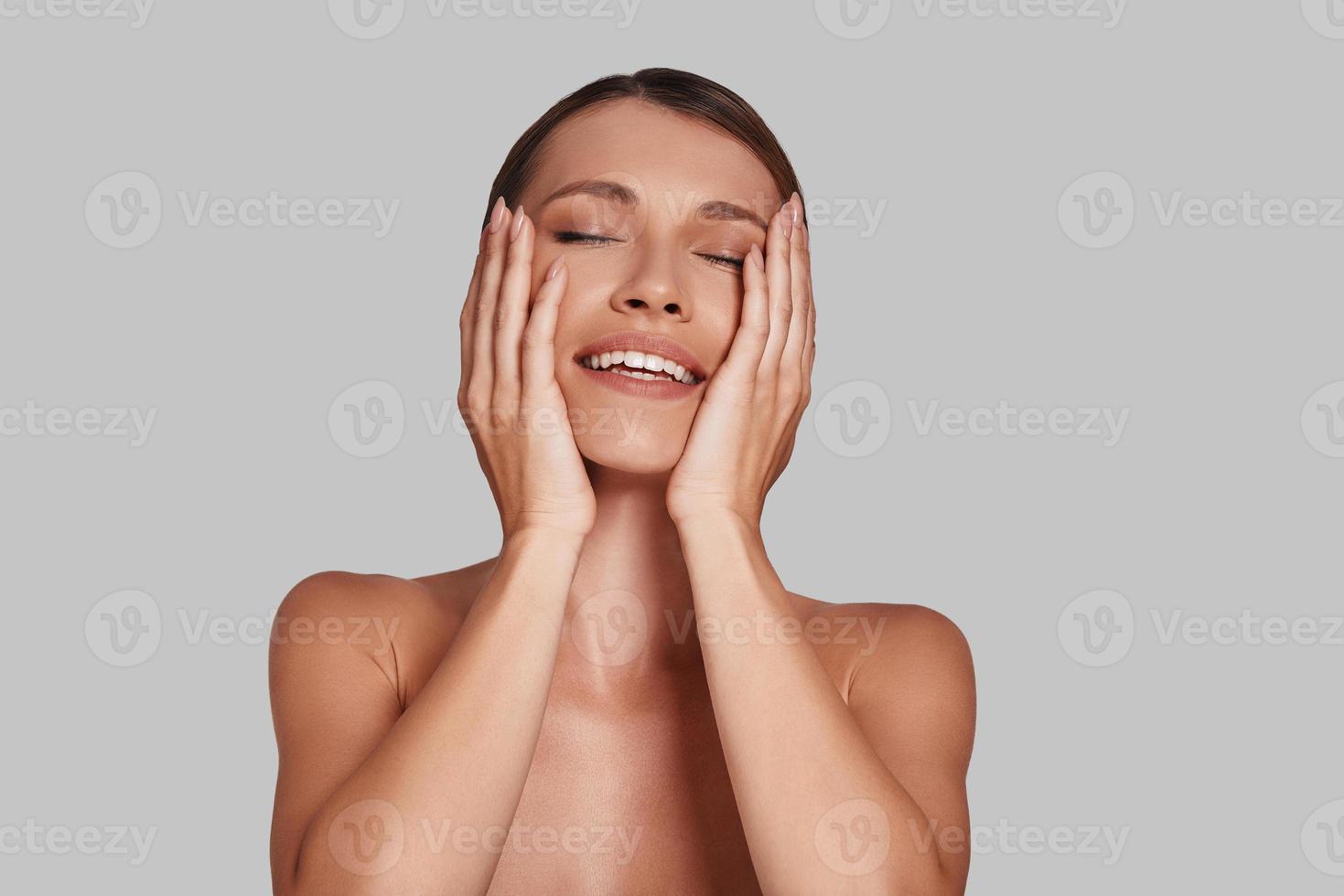 stolt till vara skön. attraktiv ung kvinna förvaring ögon stängd och leende medan stående mot grå bakgrund foto