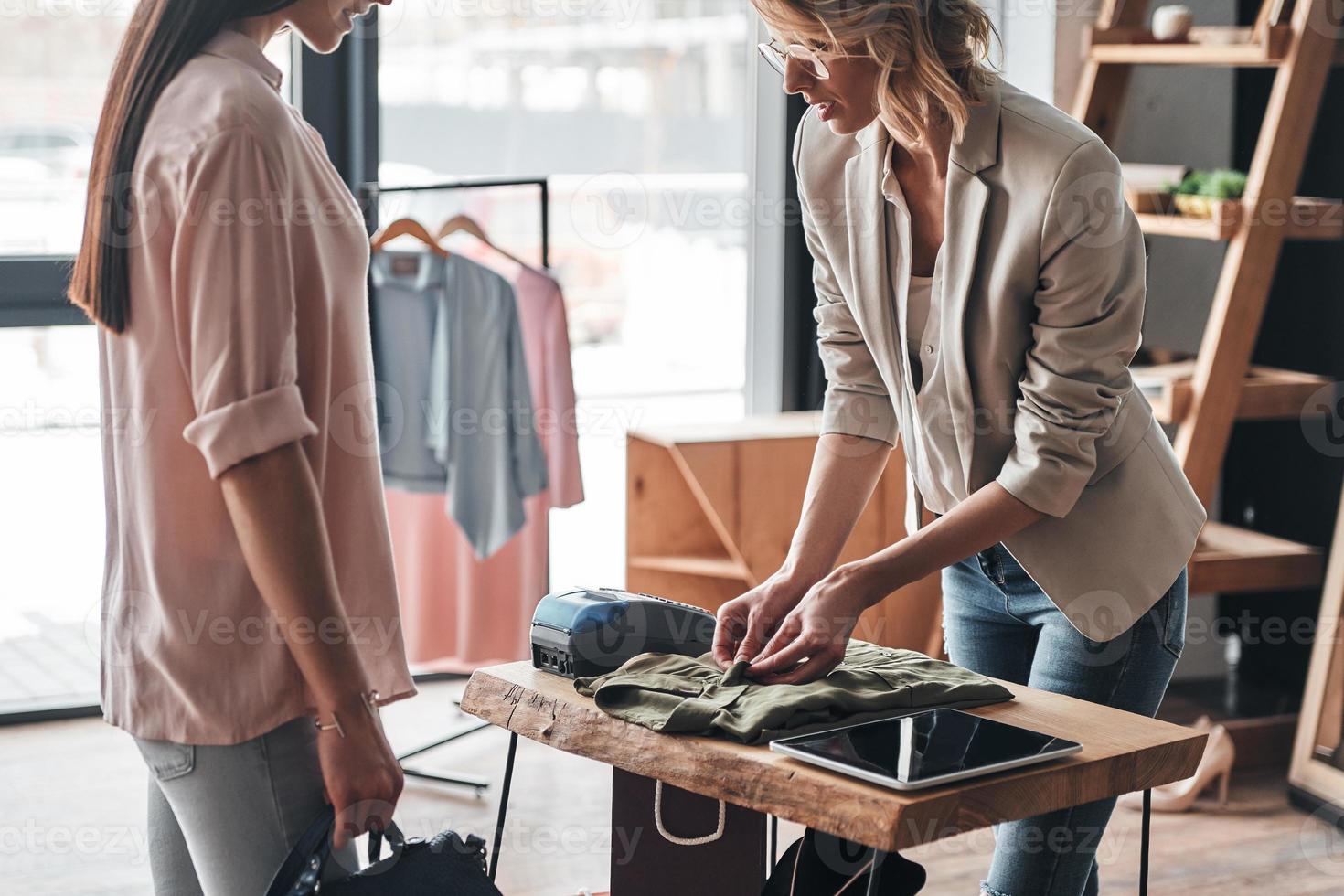 bara ett ögonblick. skön ung kvinna hopfällbar en skjorta för henne kund medan arbetssätt i de mode boutique foto