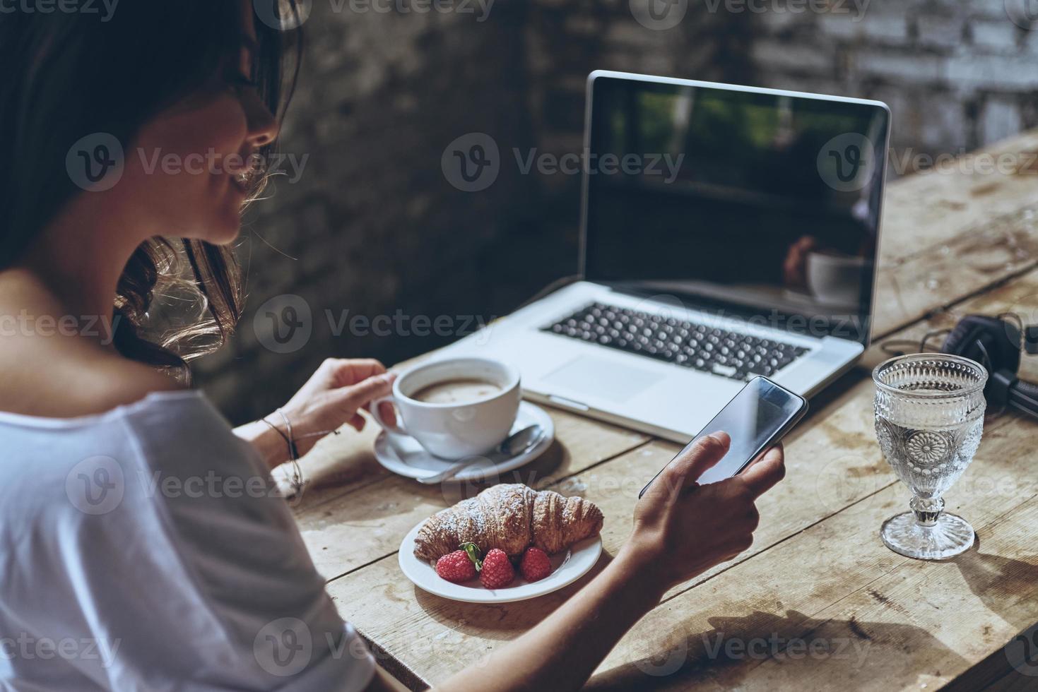 snabbt chatt på de morgon. bak- se av kvinna använder sig av smart telefon medan har frukost på Hem foto