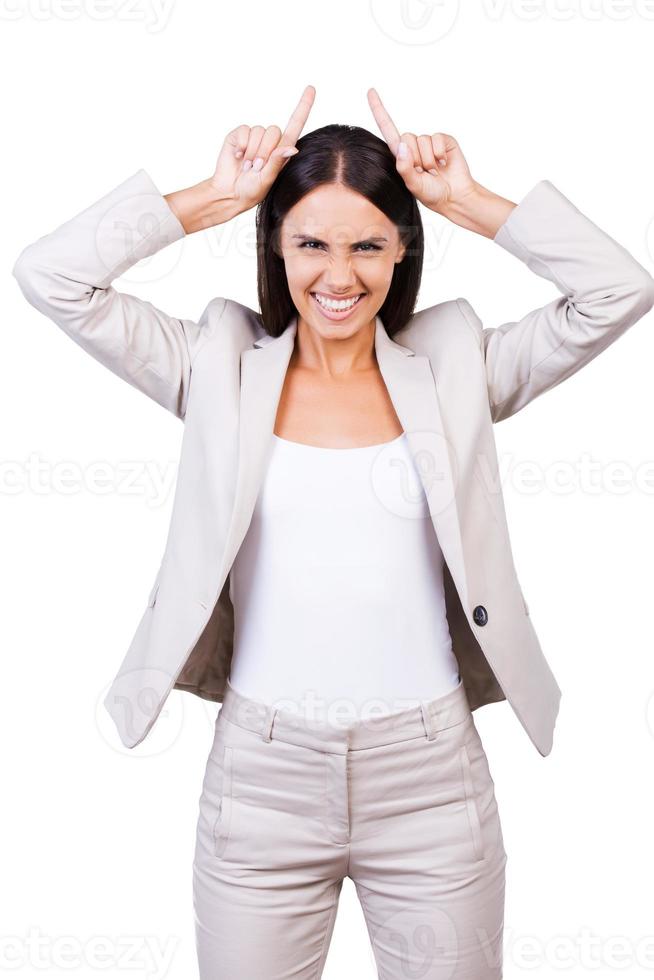 företag jäkel. lekfull ung affärskvinna i kostym framställning horn förbi fingrar och grimaserande medan stående mot vit bakgrund foto