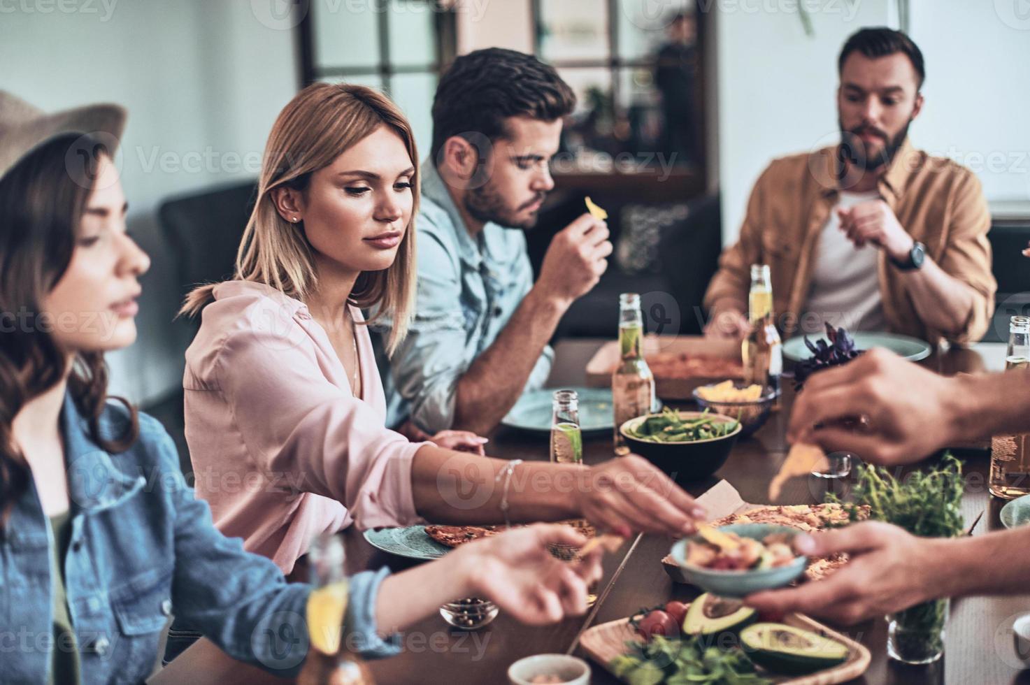 bara hungrig. grupp av ung människor i tillfällig Kläder äter medan har en middag fest inomhus foto