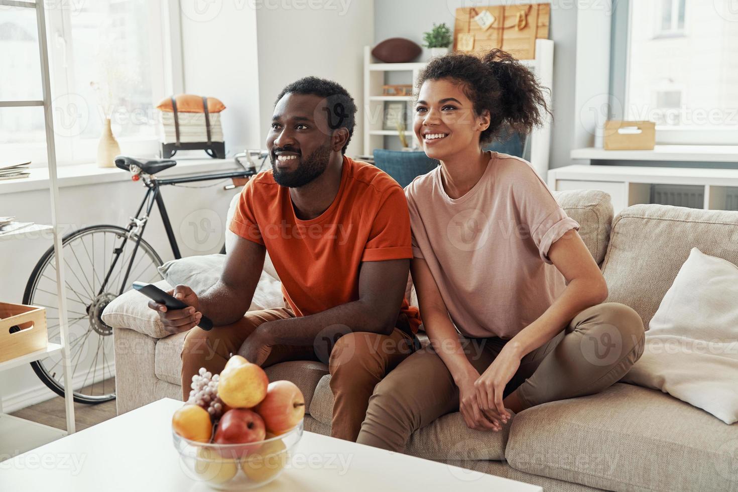 skön ung afrikansk par tittar på TV och leende medan utgifterna tid på Hem foto