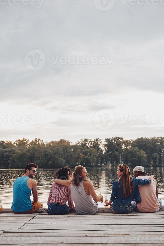 bra tid med vänner. bak- se av ung människor i tillfällig ha på sig talande och leende medan Sammanträde på de pir foto