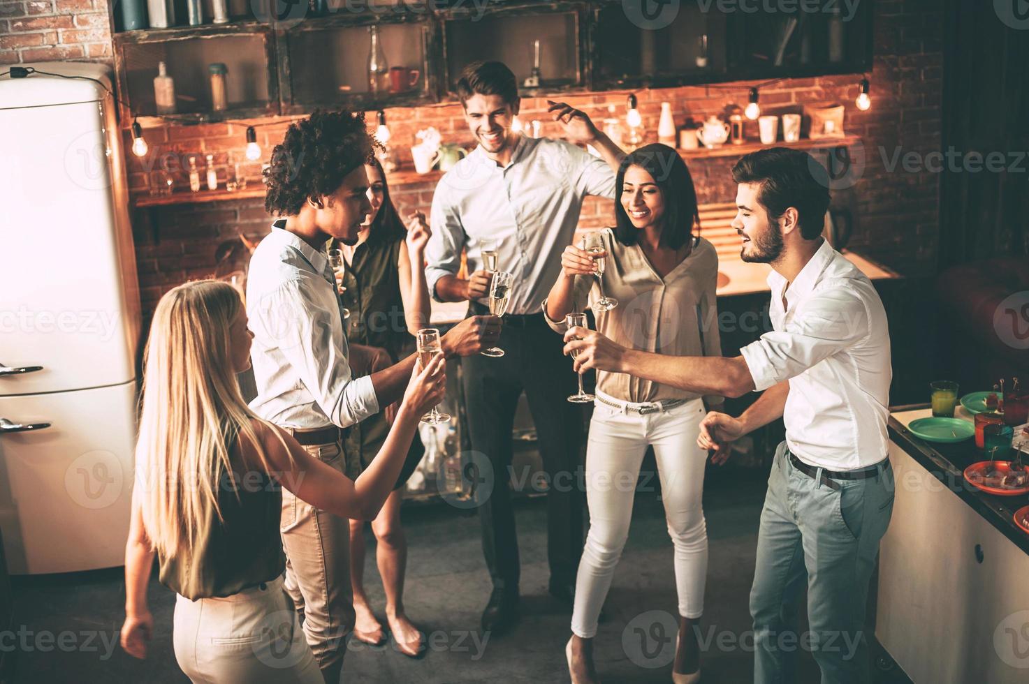 fest med bäst vänner. topp se av glad ung människor dans och dricka medan njuter Hem fest på de kök foto
