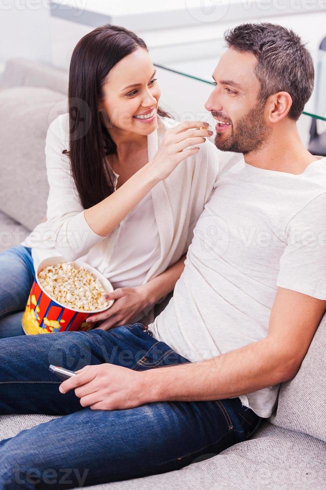 njuter sorglös tid tillsammans. skön ung kärleksfull par bindning till varje Övrig och äter popcorn medan Sammanträde på de soffa och tittar på TV foto