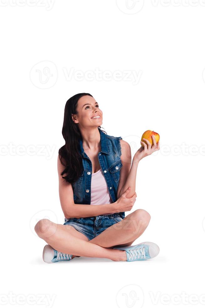 äpple tid skön ung glad kvinna innehav äpple och ser upp med leende medan Sammanträde i lotus placera mot vit bakgrund foto