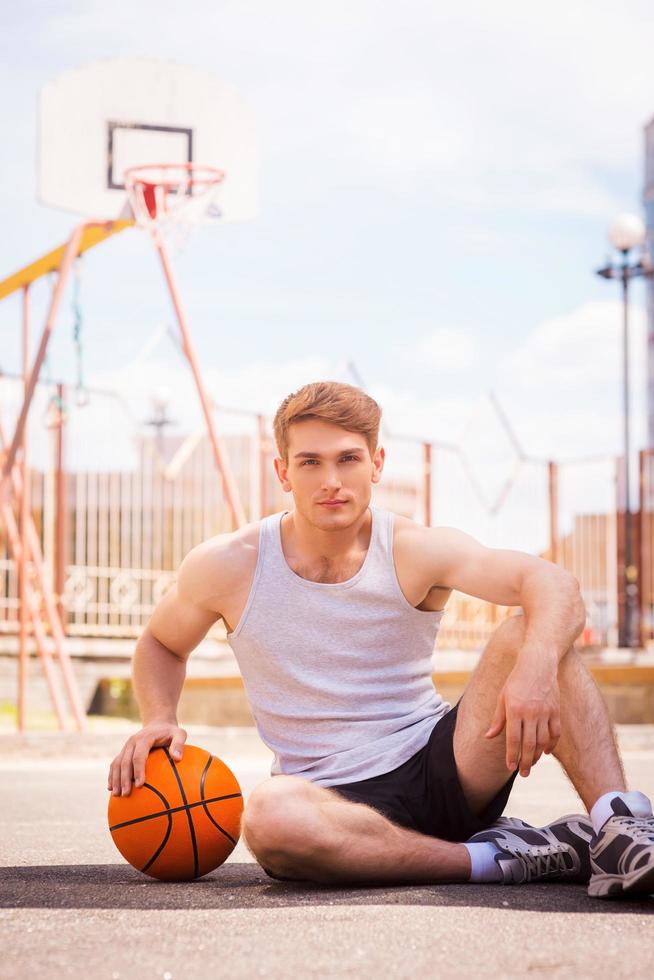 basketboll spelare. självsäker ung manlig basketboll spelare Sammanträde utomhus med boll foto