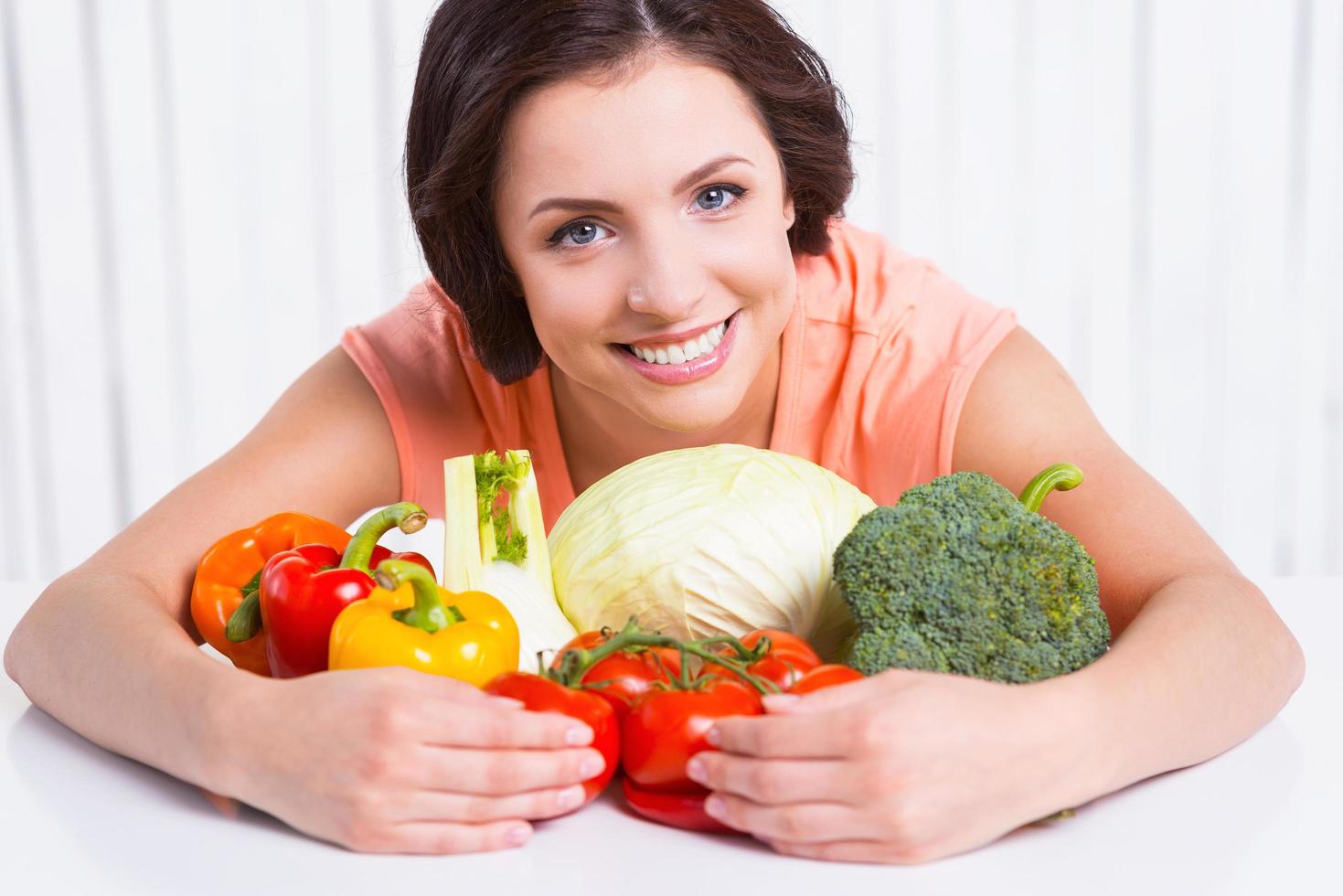 jag am vegetarian. skön ung kvinna kramas färsk grönsaker om på de tabell och leende foto