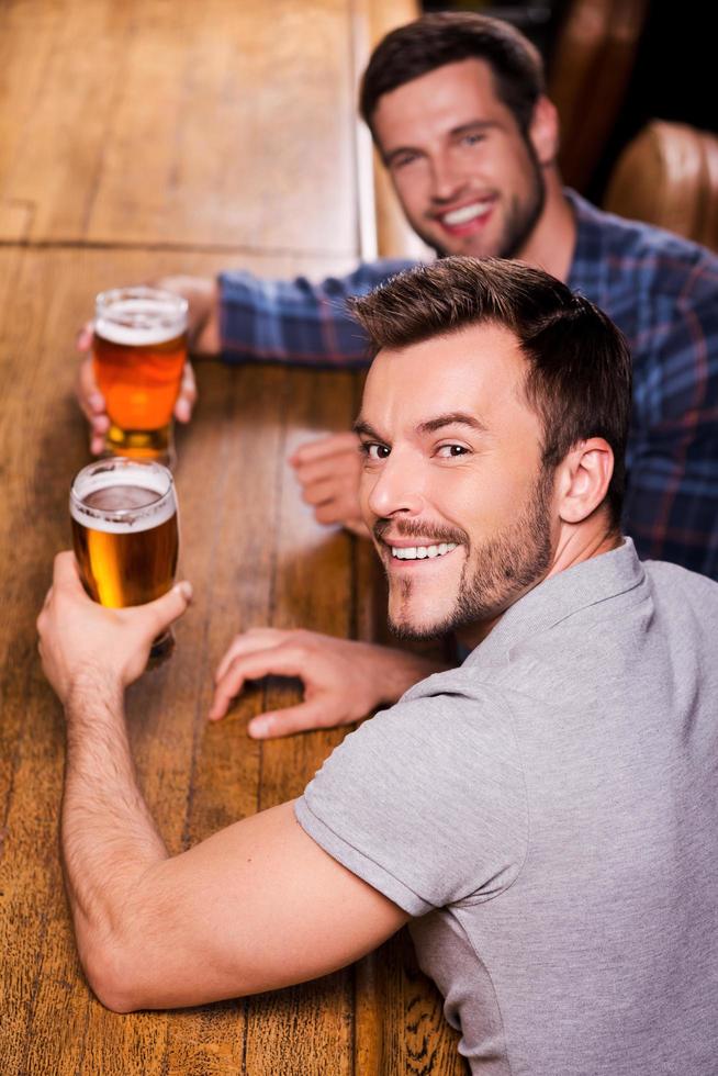 vänner i bar. topp se av två Lycklig ung män dricka öl på de bar disken och leende foto