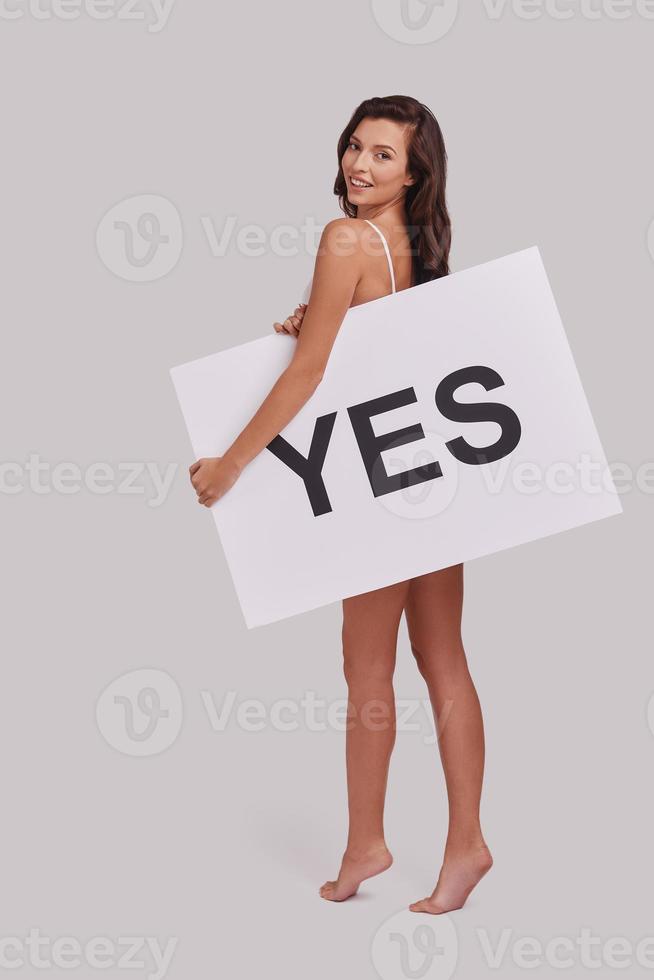 aldrig ge upp. full längd av attraktiv ung kvinna beläggning med en affisch och leende medan stående mot grå bakgrund foto