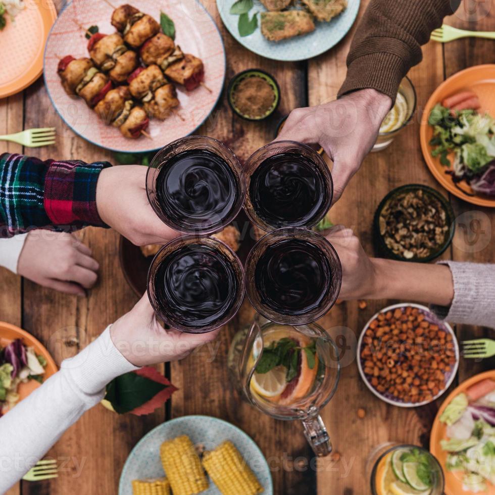 Skål till vänner topp se av fyra människor glädjande med röd vin medan Sammanträde på de rustik dining tabell foto