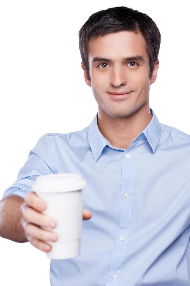 delning kaffe med du. stilig ung man i blå skjorta innehav en kaffe kopp utsträckt och leende medan stående isolerat på vit foto