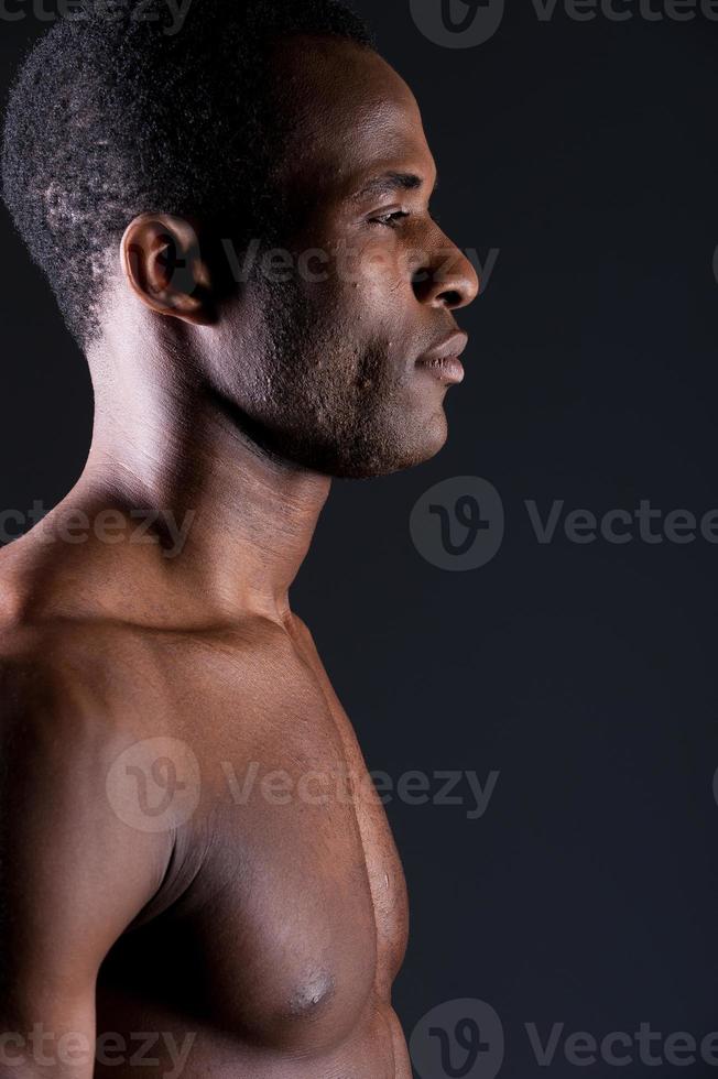 manlighet. sida se av ung afrikansk man ser bort medan stående mot grå bakgrund foto