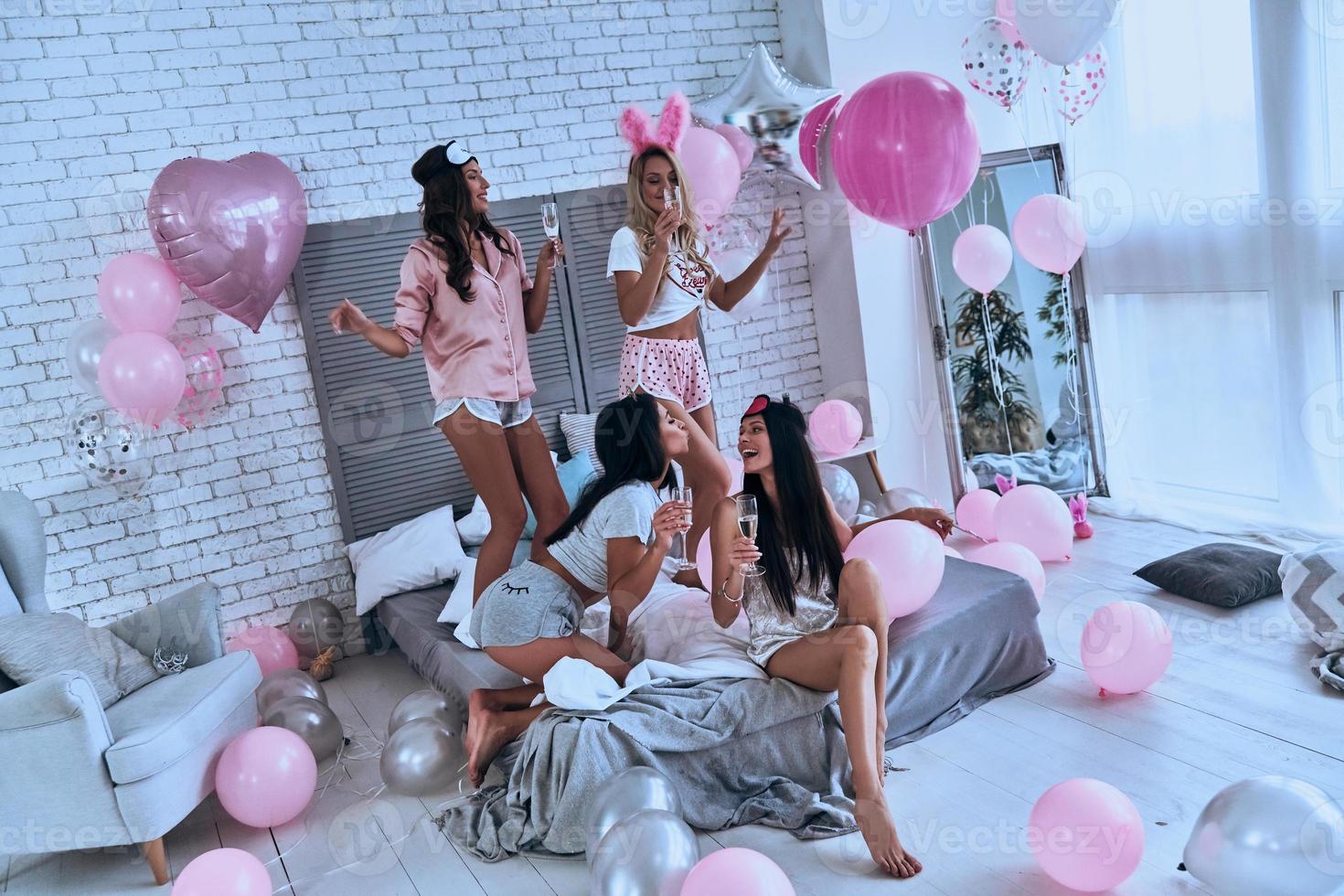 så mycket roligt fyra lekfull ung leende kvinnor i pyjamas bindning tillsammans medan har en slummer fest i de sovrum med ballonger Allt över de plats foto