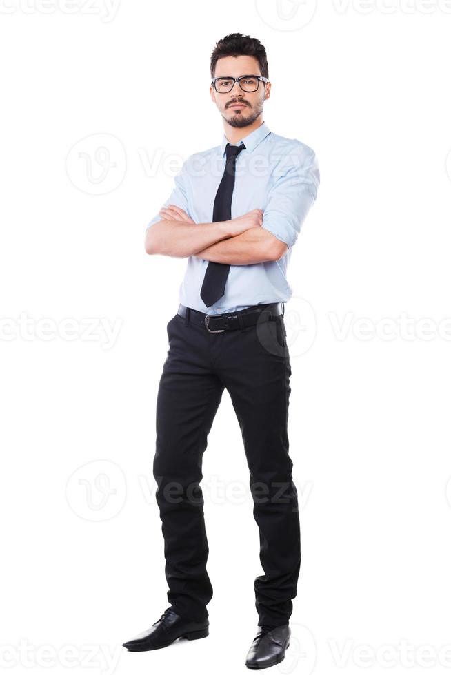 självsäker affärsman. full längd av stilig ung man i skjorta och slips förvaring vapen korsade och ser på kamera medan stående mot vit bakgrund foto