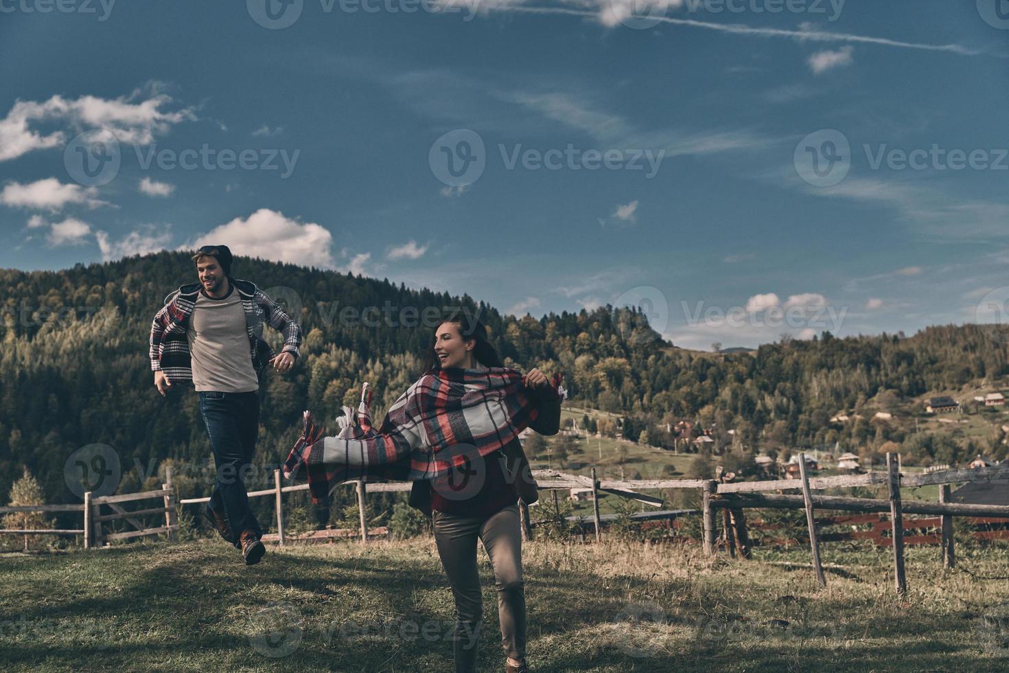 Allt de behöver är kärlek. Lycklig ung par leende medan löpning på de dal i bergen utomhus foto