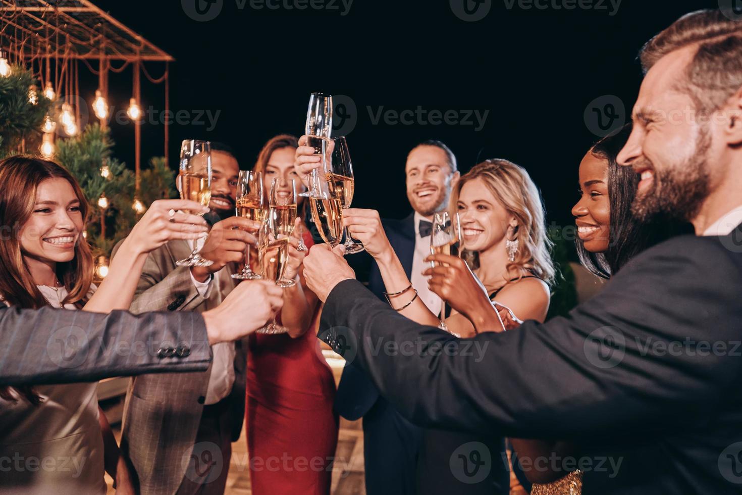 grupp av skön människor i formell klädsel toasting med champagne och leende medan utgifterna tid på lyx fest foto